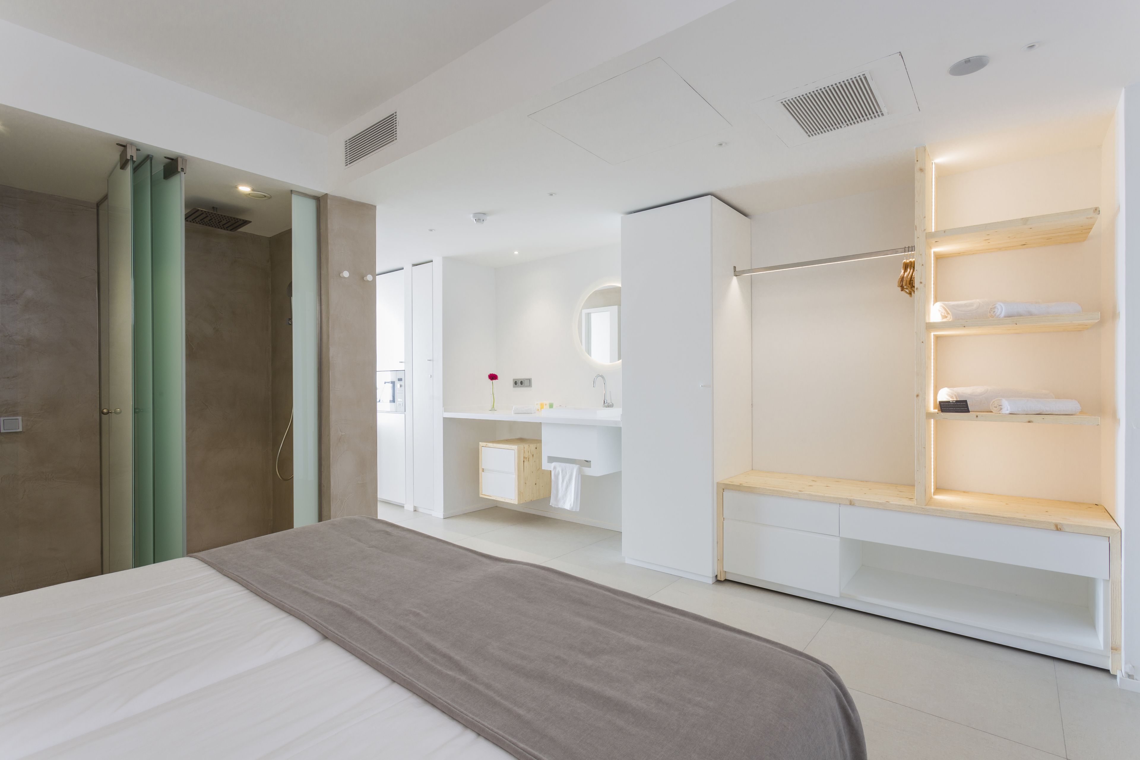 A modern hotel room with a large bed, a walk-in closet, a bathroom with a vanity, and a shower area.
