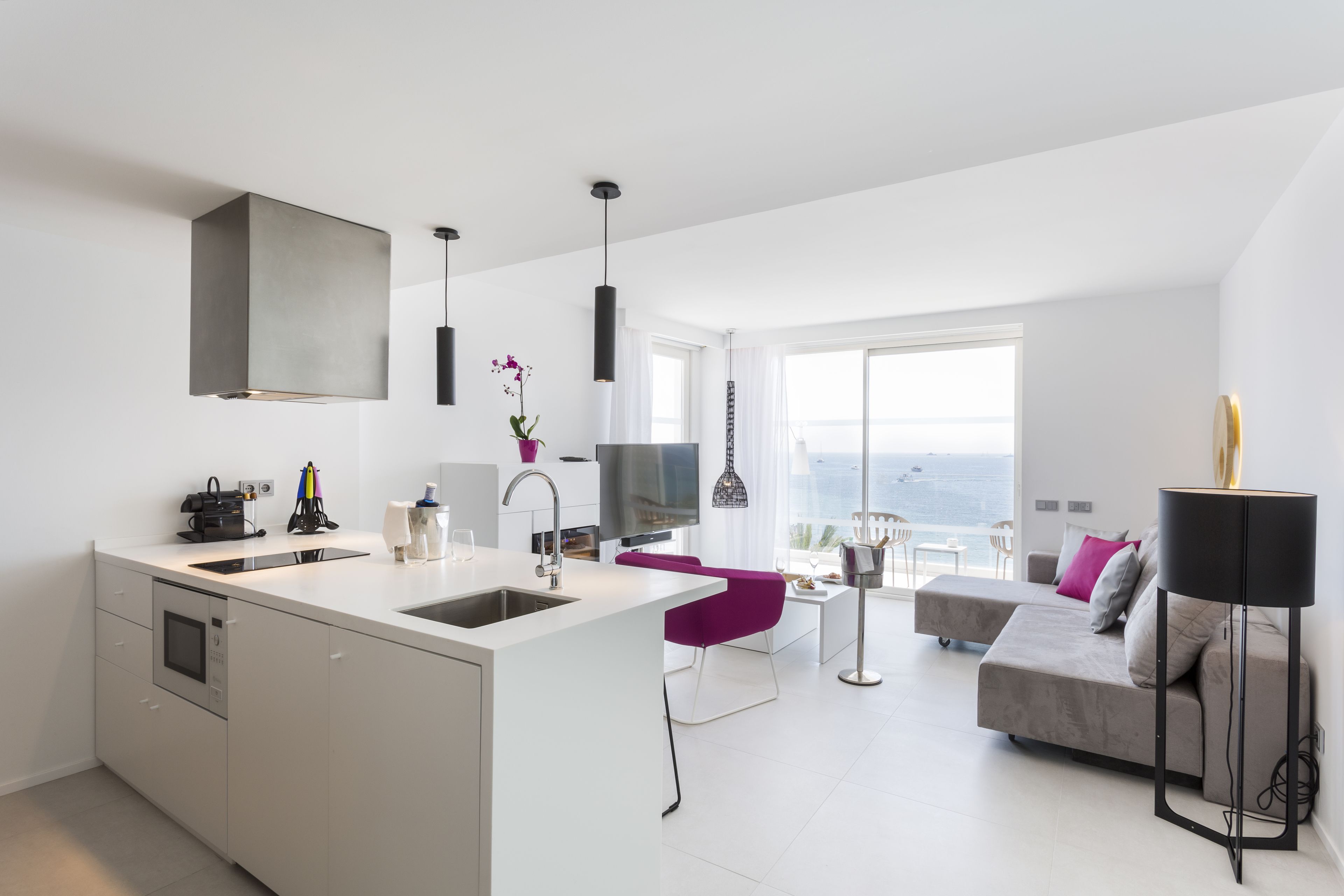 Una cocina moderna con una isla grande, un área de comedor con una silla morada, un sofá y un ventanal con vistas.