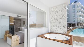 Un baño moderno con una bañera de madera, un ventanal grande y vistas a una piscina y un edificio.