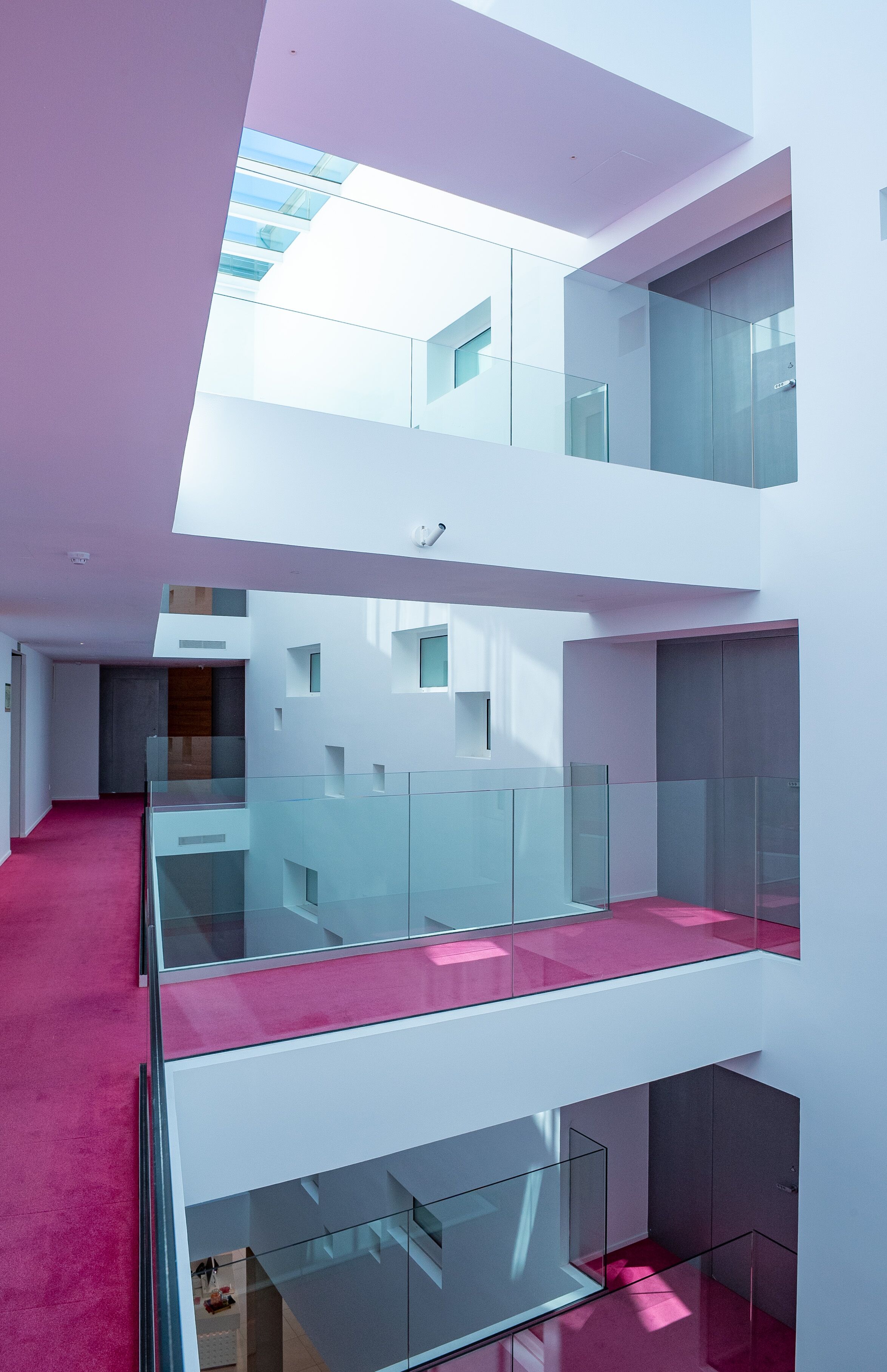 Un interior con varios niveles, barandillas de cristal y una alfombra rosa.