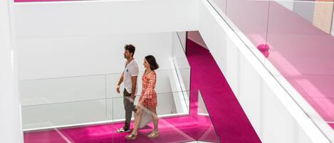 Un interior moderno con barandilla de vidrio y una pared de acento rosa.