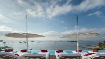 A poolside area with lounge chairs and umbrellas, overlooking a calm sea with boats.