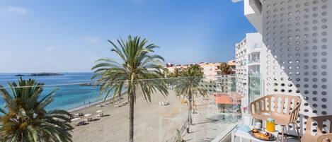 A balcony with a view of a beach, palm trees, and a clear blue sky.