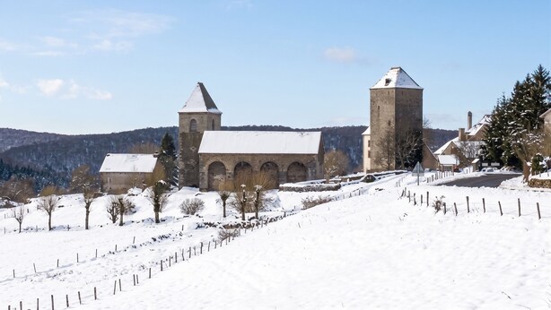 A historic building with arched windows and a tower, surrounded by snow-covered landscape and trees.