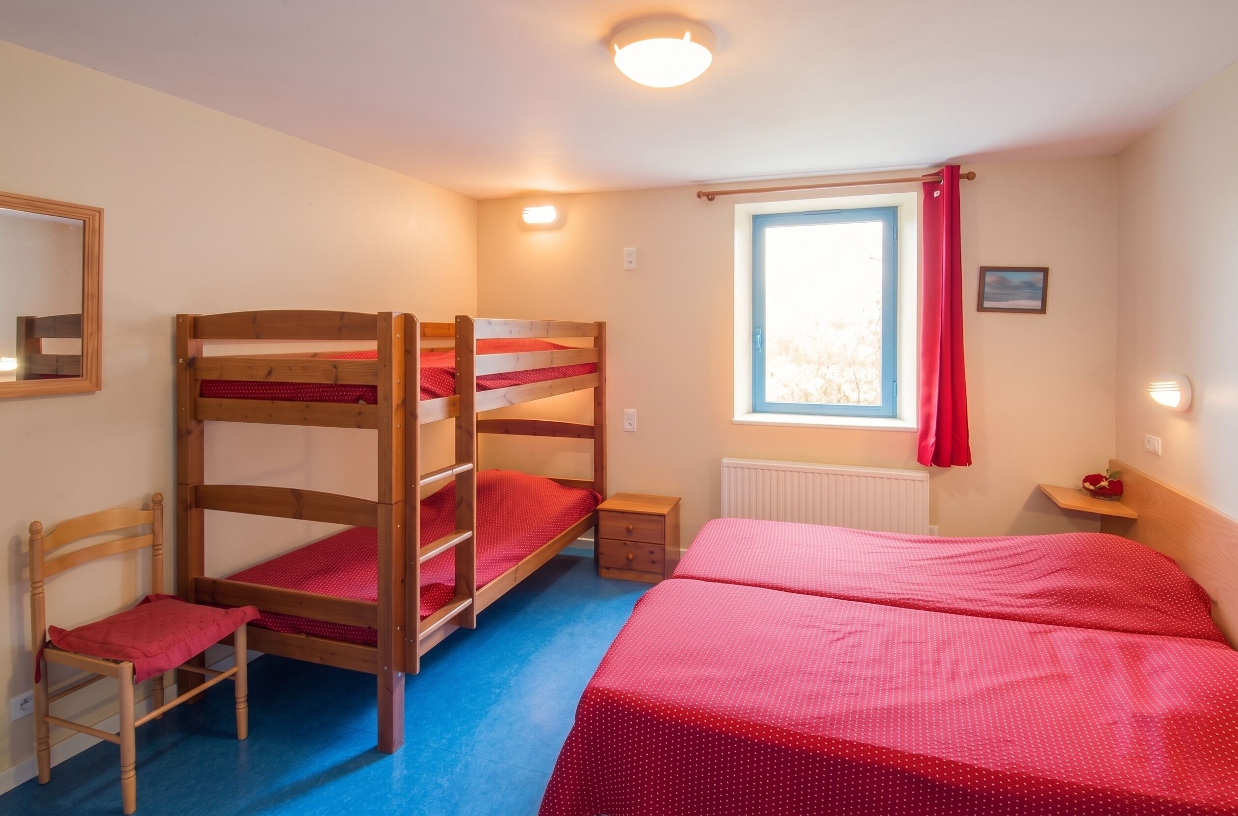 Habitación con literas, una ventana, una silla y una mesita de noche pequeña.