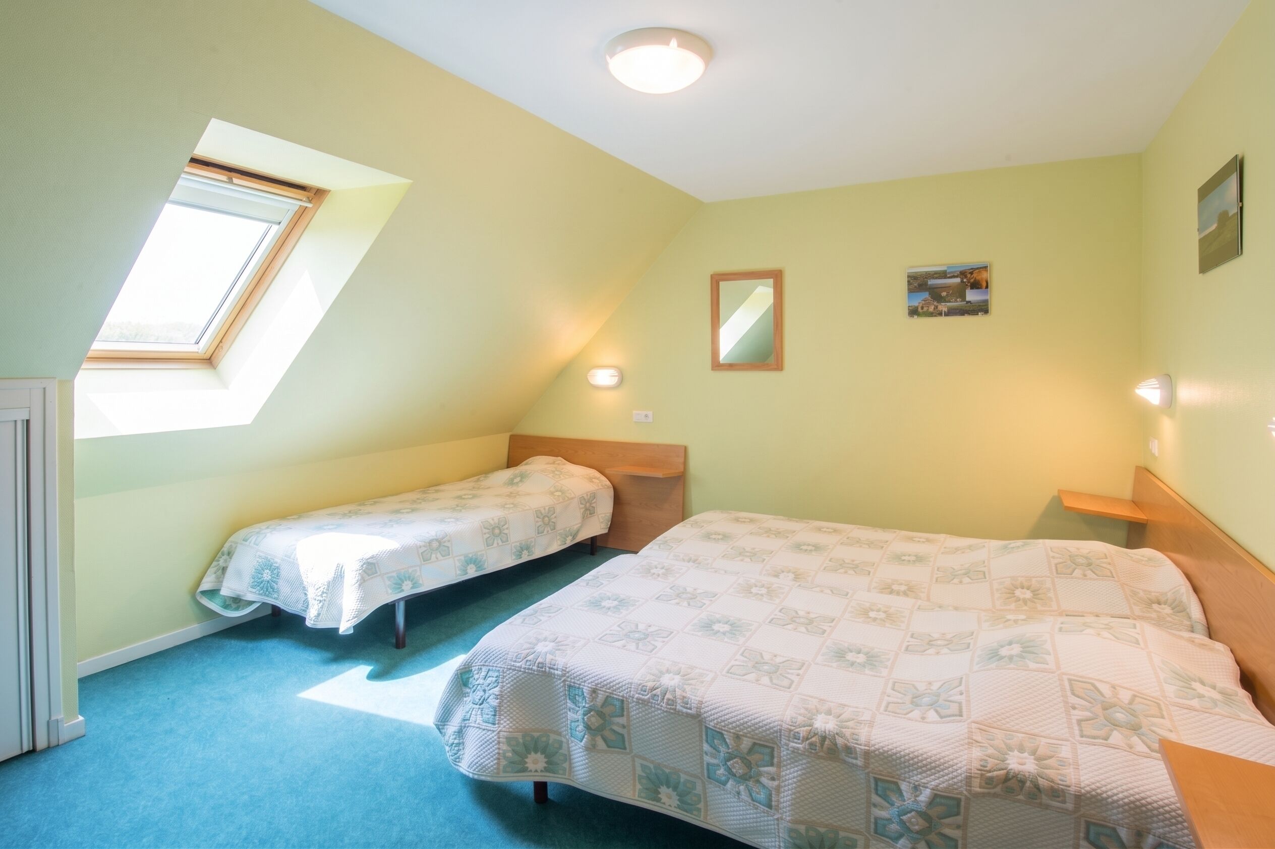Ein Zimmer mit zwei Betten, einem Oberlicht, einem kleinen Fenster und einer Wandleuchte.