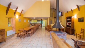 A spacious dining area with a long wooden table and chairs, a central seating area with a sofa and armchair, and a kitchen in the background.