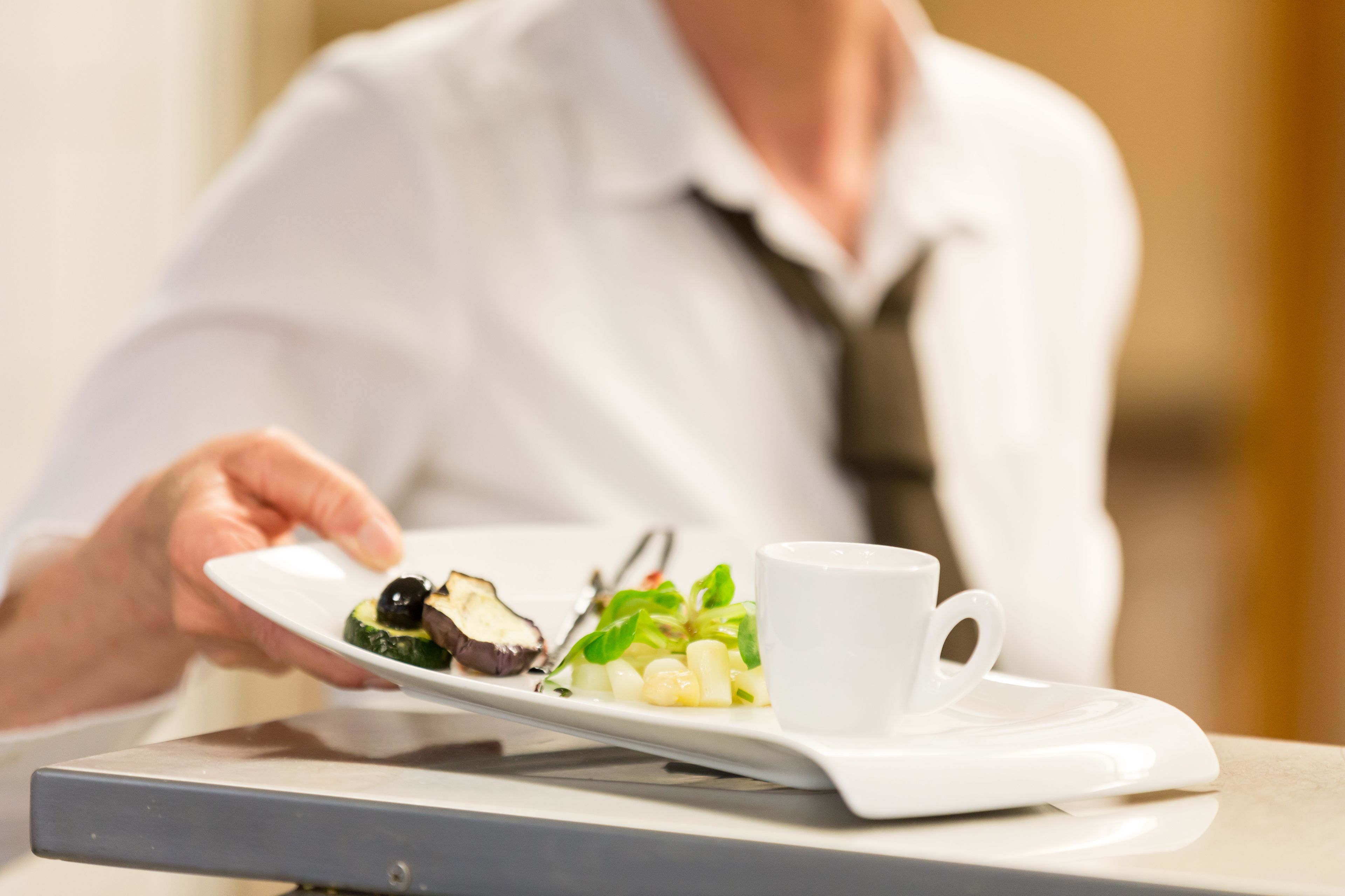 A person holding a white plate with food and a white cup on a tray.