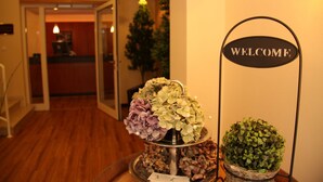 A reception area with a 'Reception' sign, a welcome sign, and a table with a floral arrangement and a small potted plant. - Landhaus Jaegerkrug (Paderborn)