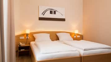 A hotel room with two single beds, a bedside table with a lamp, a phone, and a wall-mounted artwork.