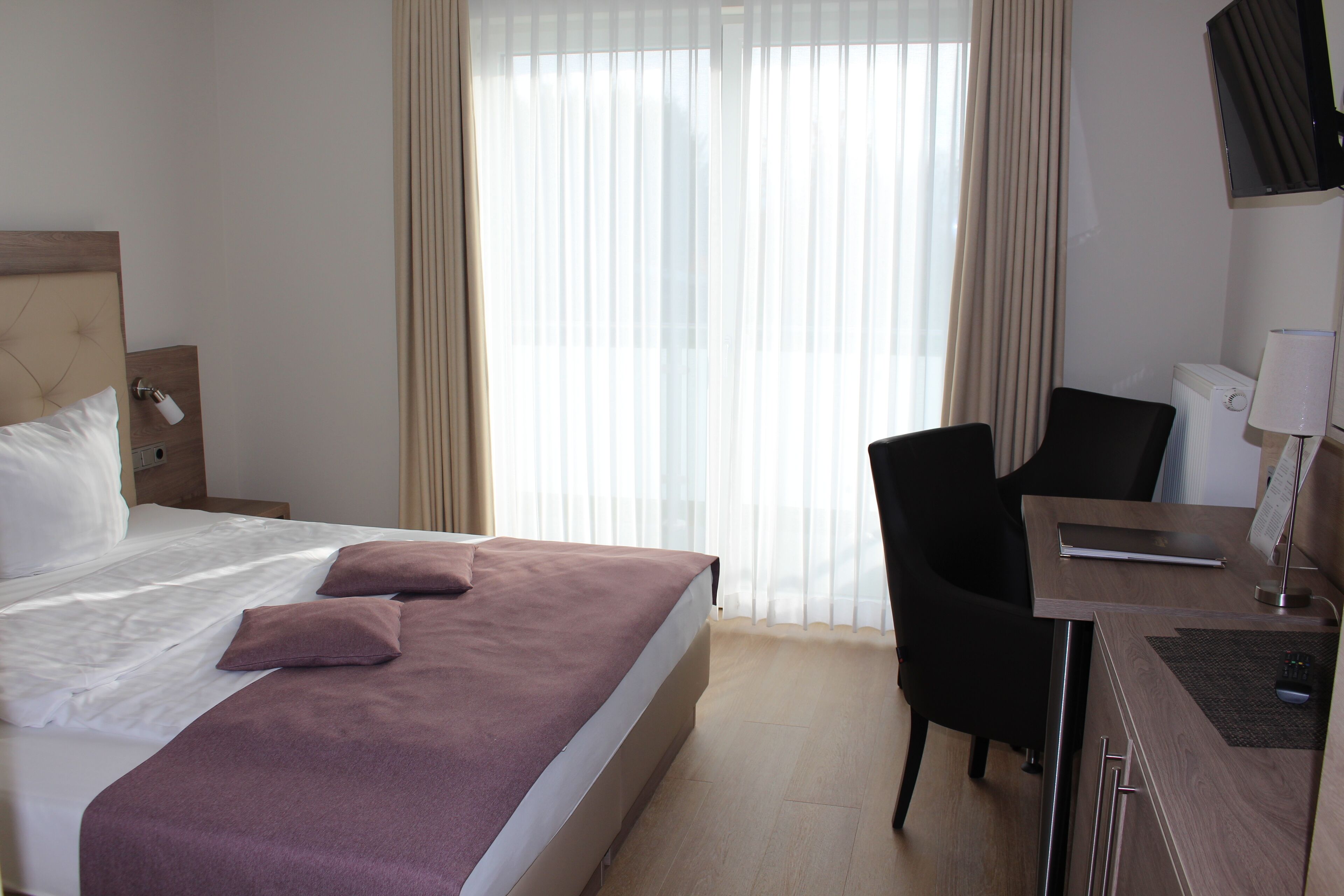 A hotel room with a bed, a desk, a chair, and a TV.