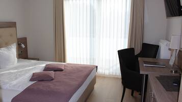 A hotel room with a bed, a desk, a chair, and a TV.