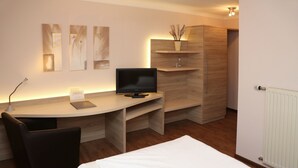 A modern hotel room with a wooden desk, a black chair, a bed, and a TV. - Landhaus Jaegerkrug (Paderborn)