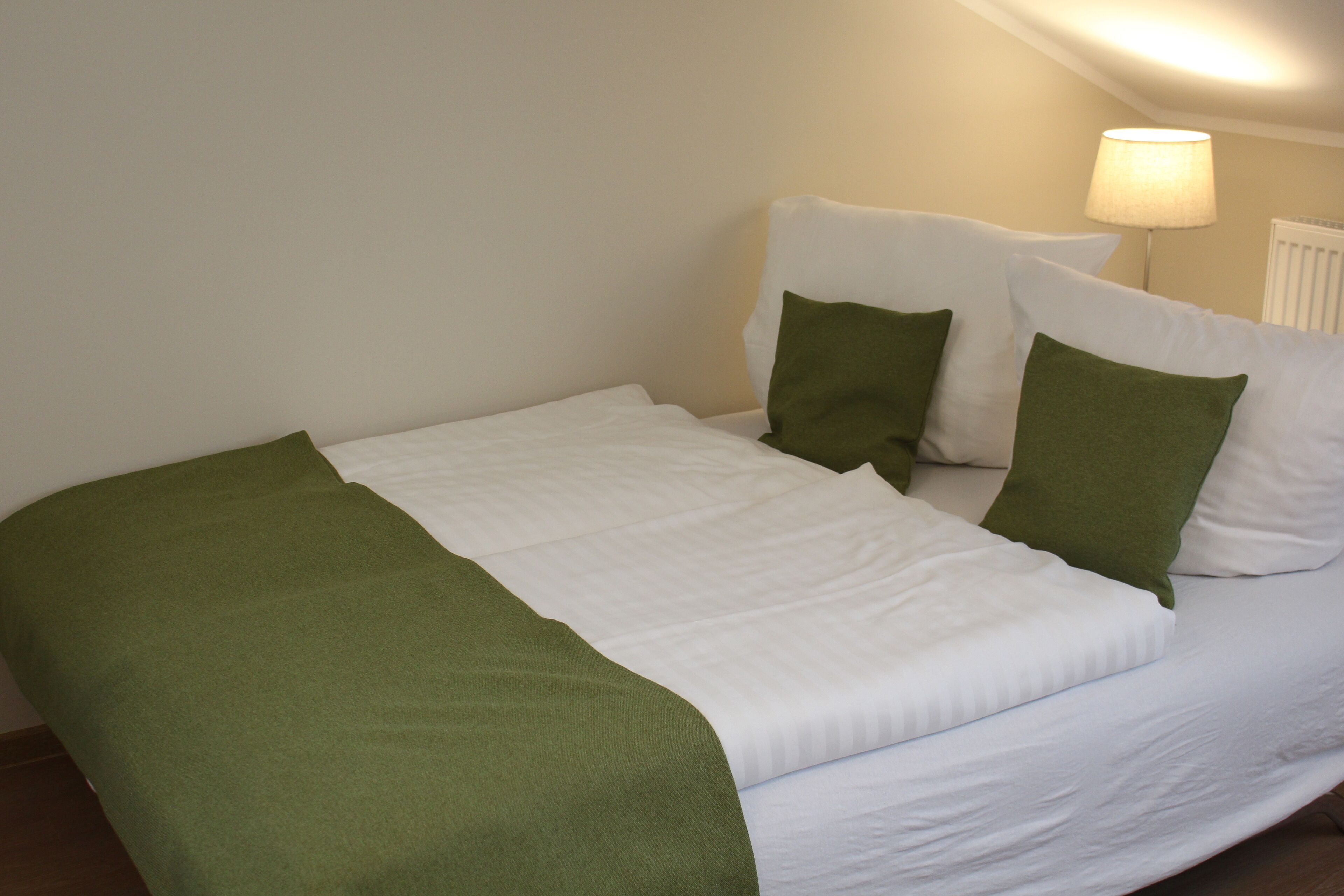 A neatly made bed with white bedding and green pillows, a green throw blanket, and a lamp on a bedside table.