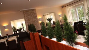 A modern interior with a stone accent wall, wooden seating, and potted plants. - Landhaus Jaegerkrug (Paderborn)