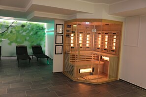 A room with a corner fireplace, two lounge chairs, and a wall with a leaf pattern. - Landhaus Jaegerkrug (Paderborn)