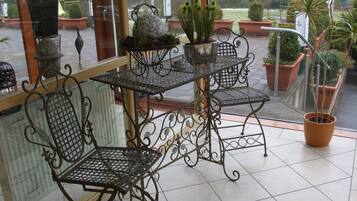 A patio area with a table and two chairs, surrounded by potted plants and a view of the garden.