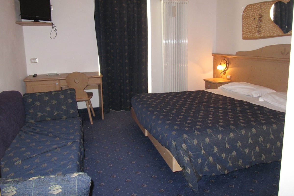 A hotel room with two beds, a desk, a chair, a television, and a window with curtains.