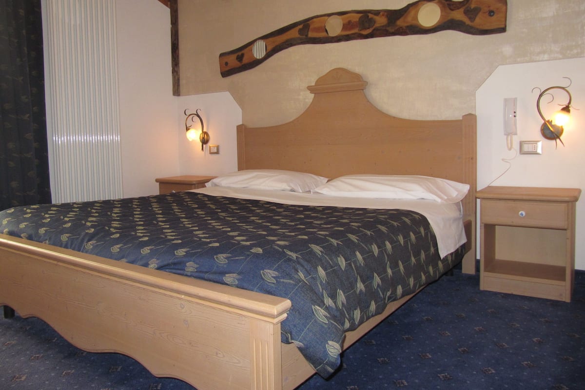 A bedroom with a wooden bed, two bedside tables, a wall-mounted lamp, and a radiator.