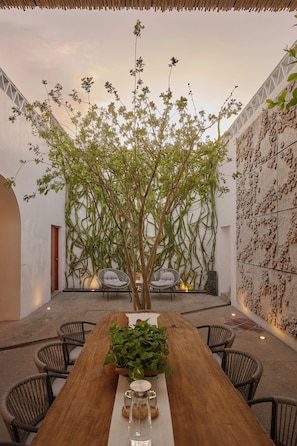 A wooden dining table with chairs, a potted plant, and a wall with a textured pattern. - Casa Carmen Morelos (Oaxaca)