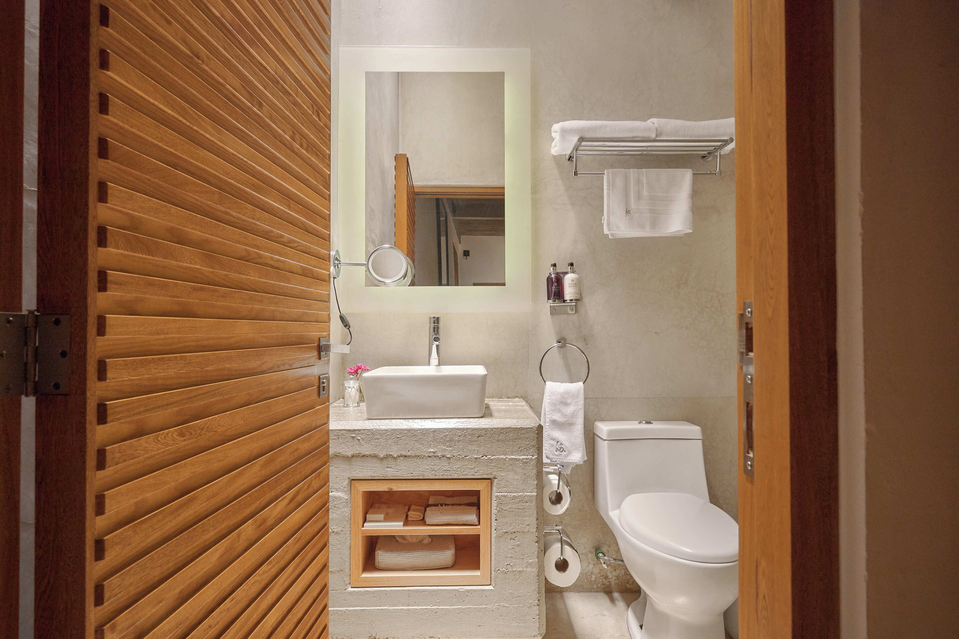 A modern bathroom with a wooden slatted wall, a sink, a toilet, and a mirror.