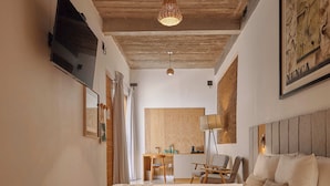A bedroom with a large bed, wooden ceiling, a TV mounted on the wall, a desk with a chair, and a lamp. - Casa Carmen Morelos (Oaxaca)