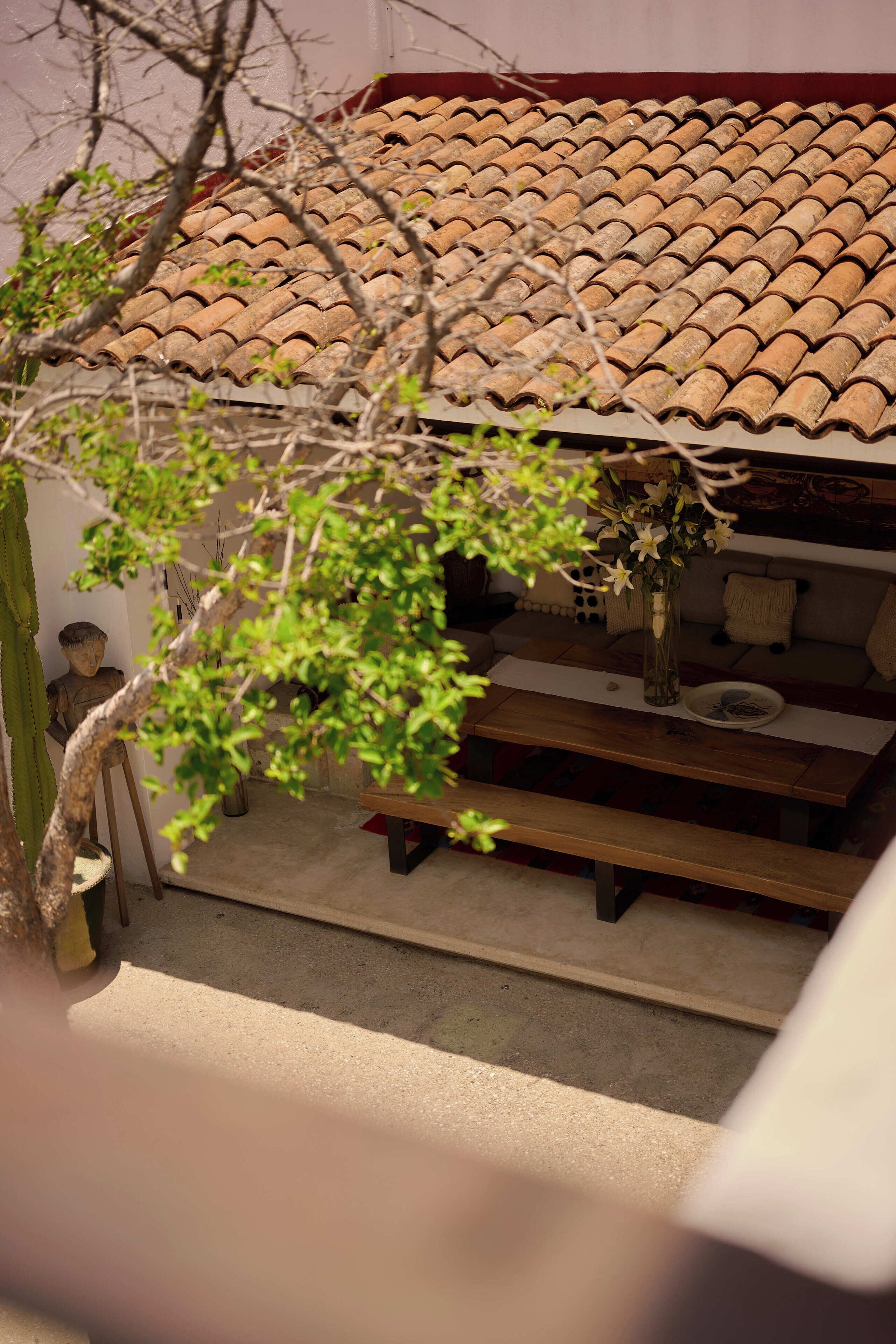 A patio area with a tiled roof, a wooden bench, a small table with a vase, and a statue.