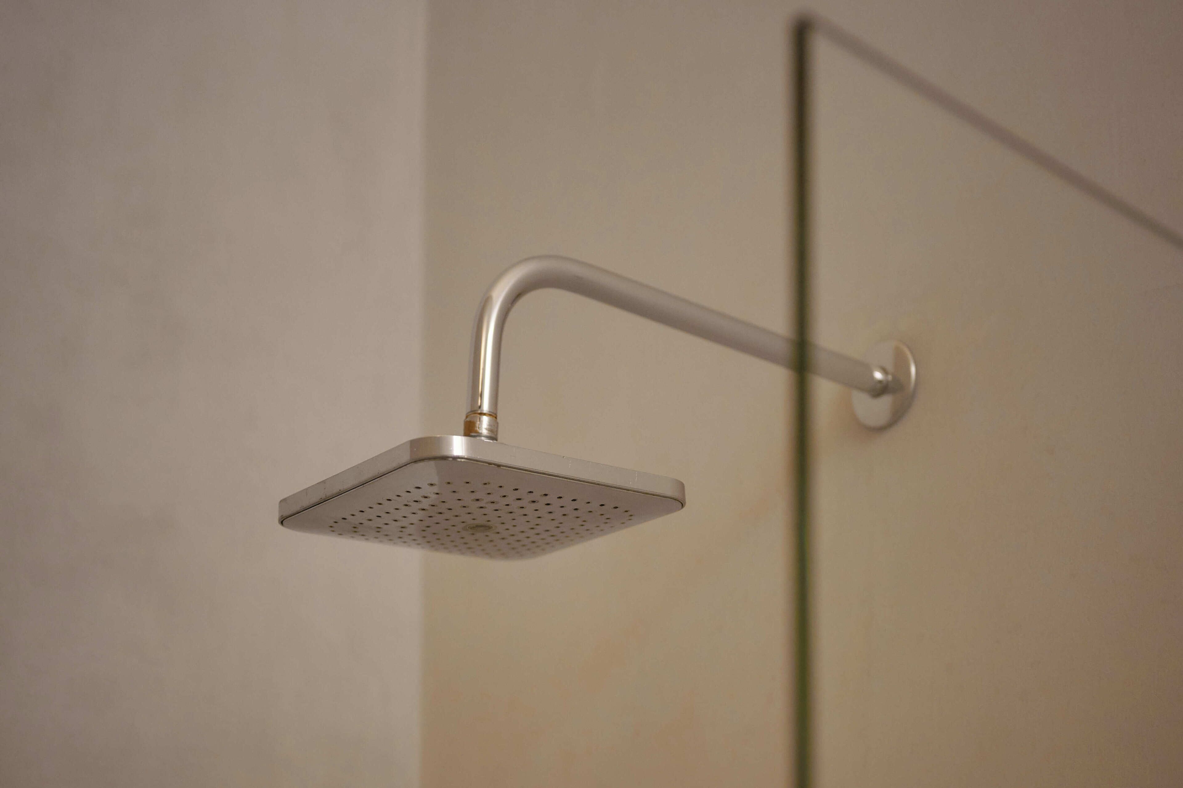 Un pommeau de douche fixé au mur, doté d’une poignée incurvée et d’une forme carrée perforée.
