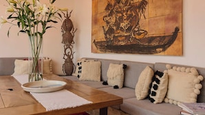 A living room with a wooden ceiling, a large abstract painting, a sofa with patterned cushions, a coffee table with a vase of flowers, and a colorful rug. - Casa Carmen Morelos (Oaxaca)