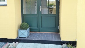 Ein gelbes Gebäude mit einer grünen Doppeltür, Hausnummer 74, und einem kleinen Topfpflanzen nebenan.
