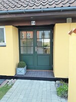 A yellow building with a green double door, number 74, and a small potted plant beside it.
