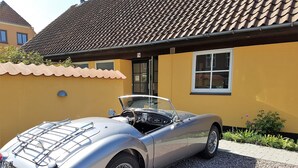 Ein klassischer Oldtimer-Cabriolet vor einem gelben Gebäude mit einem Ziegeldach.