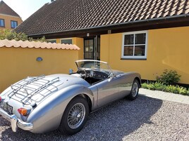 Ein klassischer Oldtimer-Cabriolet vor einem gelben Gebäude mit einem Ziegeldach.