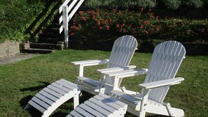 Zwei Adirondack-Stühle mit angebrachten Bänken in einer grünen Außenanlage.