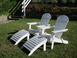 Zwei Adirondack-Stühle mit angebrachten Bänken in einer grünen Außenanlage.