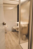 Casa de banho moderna com sanita, dispensador de papel e cabine de duche em vidro.