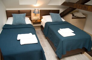 Quarto de hotel com duas camas, cada uma com colcha verde-água e travesseiros brancos, mesa de cabeceira com abajur e cabeceira de madeira.