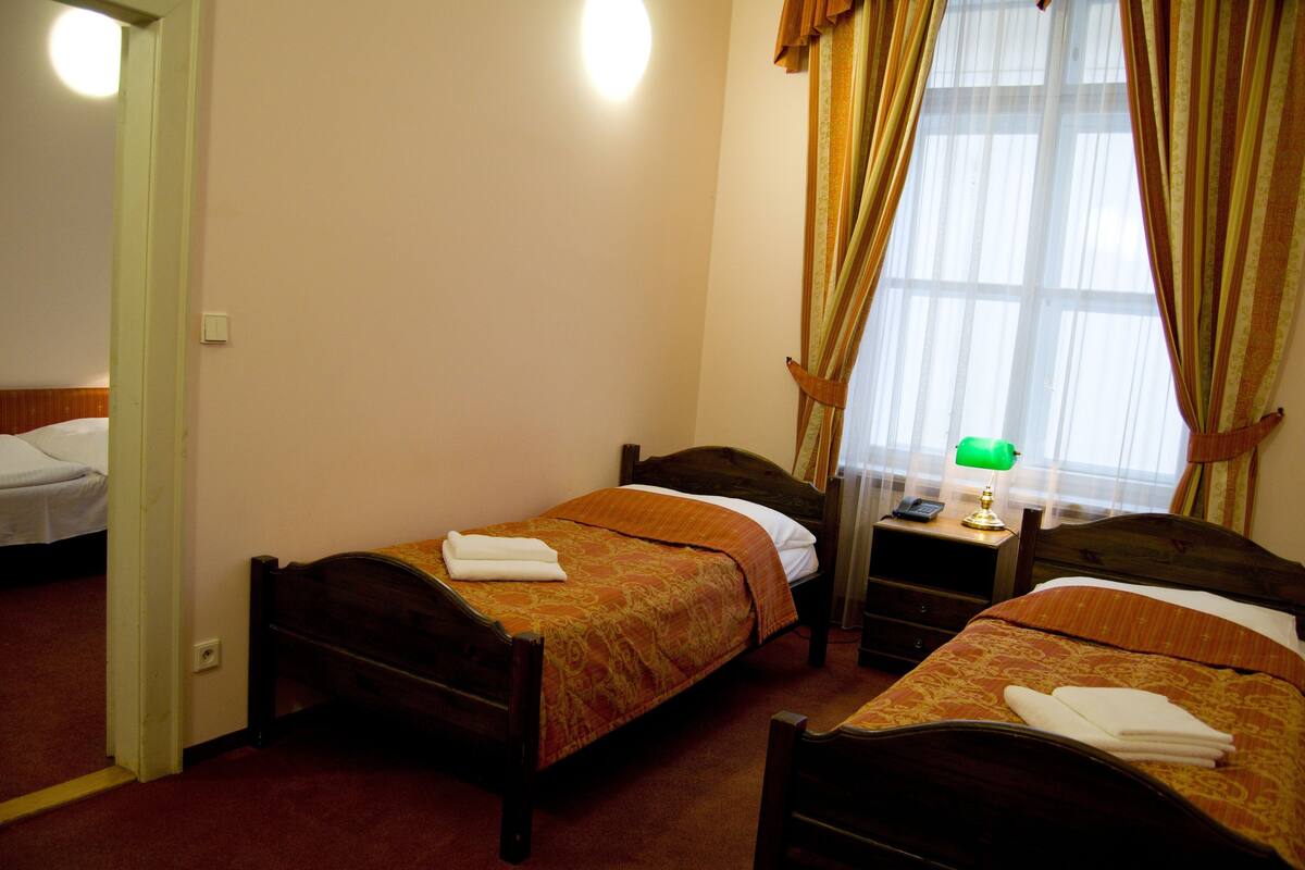 A hotel room with two single beds, a bedside table with a lamp, and a window with curtains.