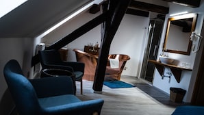 Une chambre de style loft moderne, avec un plafond en pente, une grande fenêtre, une baignoire et une salle de bain équipée d’un miroir et d’un lavabo.