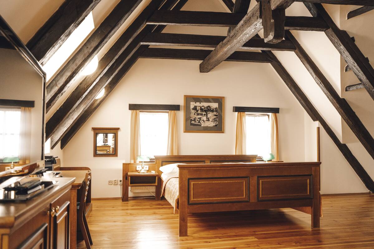 A bedroom with a wooden bed, a nightstand, a desk, and a window with curtains.