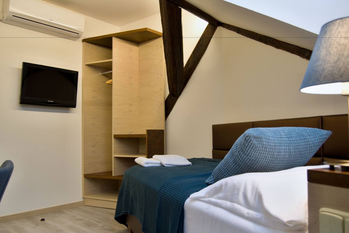 A bedroom with a bed, a TV mounted on the wall, and a wooden shelving unit.