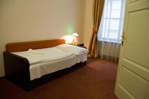 Uma cama bem arrumada com lençóis brancos, uma mesa de cabeceira com abajur e uma janela com cortinas.