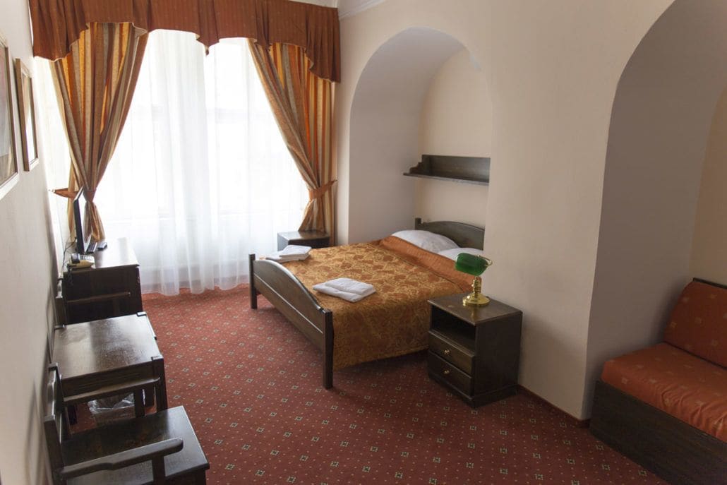 Une chambre à coucher comprenant un lit, un bureau, une chaise, une table de chevet et une fenêtre avec des rideaux.