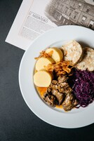 Prato de comida com bolinhos, carne e repolho roxo sobre uma superfície escura.
