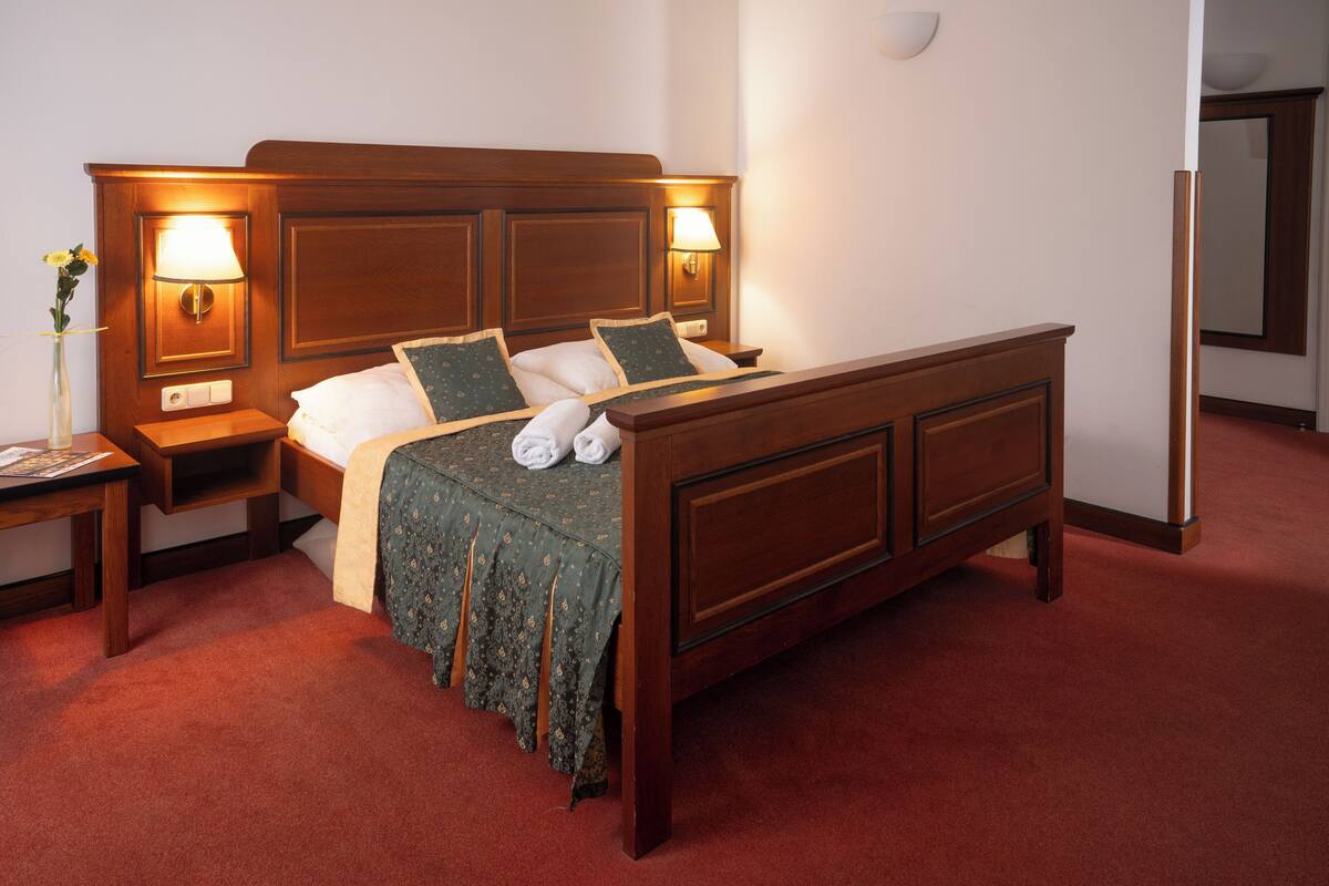 A neatly made bed with a wooden headboard, two bedside tables with lamps, and a vase with flowers on one table.