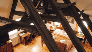 Une pièce avec un plafond en pente, des poutres en bois, un lit, un bureau et une fenêtre.