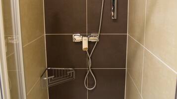 A shower area with a handheld showerhead, a wall-mounted faucet, and a small metal shelf.