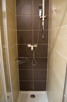 Zona de ducha con cabezal de ducha de mano, grifo empotrado en la pared y un pequeño estante metálico.
