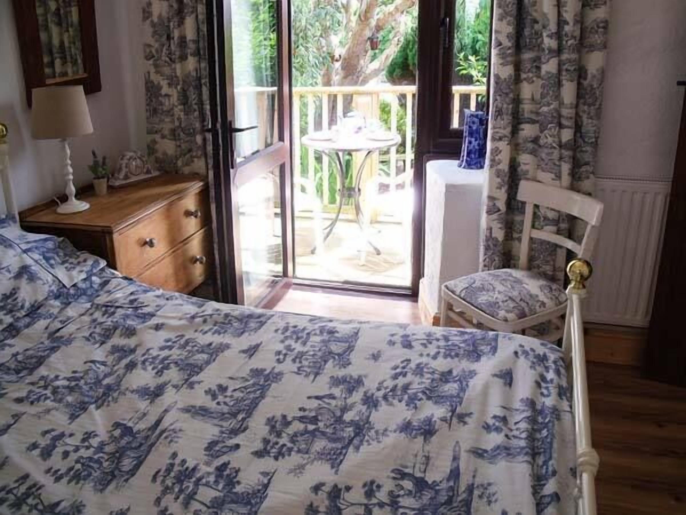 Ein Schlafzimmer mit einem Bett, einem Nachttisch, einem Sessel und Blick ins Freie.