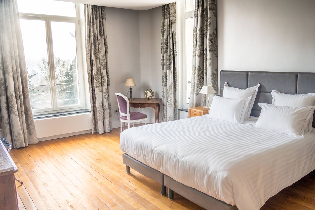 Une chambre avec un grand lit, un bureau avec une chaise, une table de chevet et une fenêtre avec des rideaux.